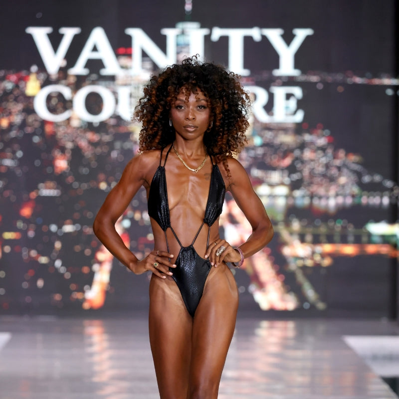 A beautiful tanned model walking down a runway during Miami Swim Week for the brand vanity couture wearing a scrappy black snake print one piece swimsuit.