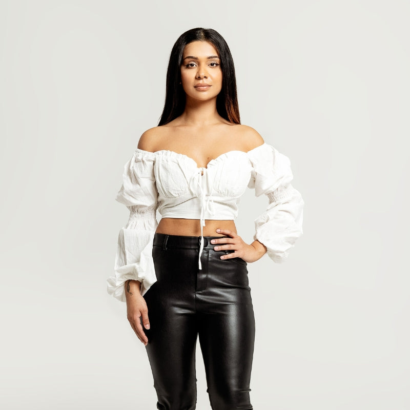 A beautiful model standing in a photography studio wearing an oversized white cropped blouse and leather pants by Vanity Couture